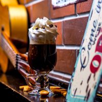 side view of irish coffee with whipped cream decorated with chocolate chips on brick wall background